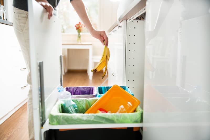 Woman putting banana peel in recycling bio bin in the kitchen.