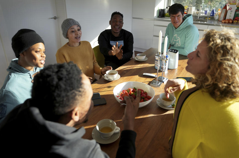 Shalom Odion, from left, Emmanuel Oyedele, Deborah Samuel, Kurrah David, host Christian Vollmann and his wife Nina Vollmann have a cup of tea after an interview with The Associated press in Gross Koeris near Berlin, Germany, Monday, March 7, 2022. Christian Vollmann offered his holiday home until the end of April to the Nigerian students who fled Kyiv after the Russian attack on Ukraine. (AP Photo/Michael Sohn)