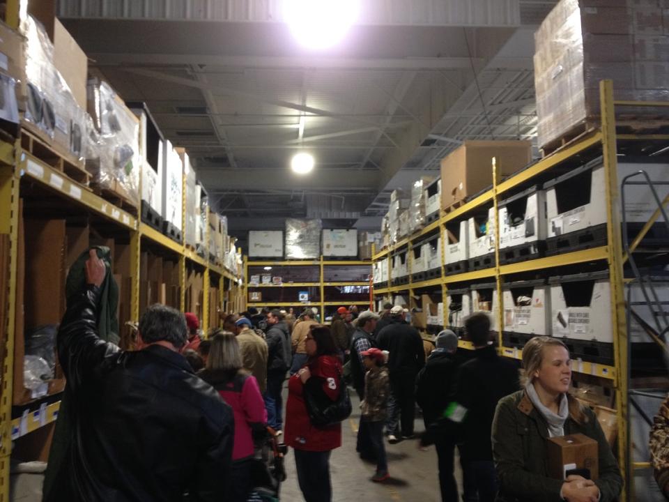 Shoppers in an aisle in a warehouse with shelves to the ceiling with products.