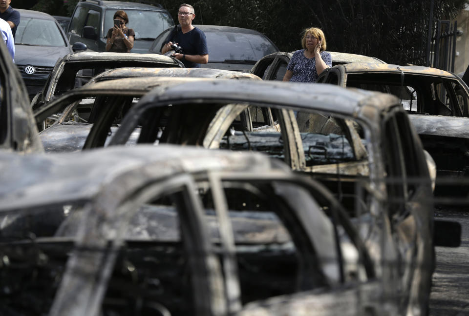 <p>People stand amid the charred remains of burned-out cars in Mati east of Athens, Tuesday, July 24, 2018. (Photo: Thanassis Stavrakis/AP) </p>