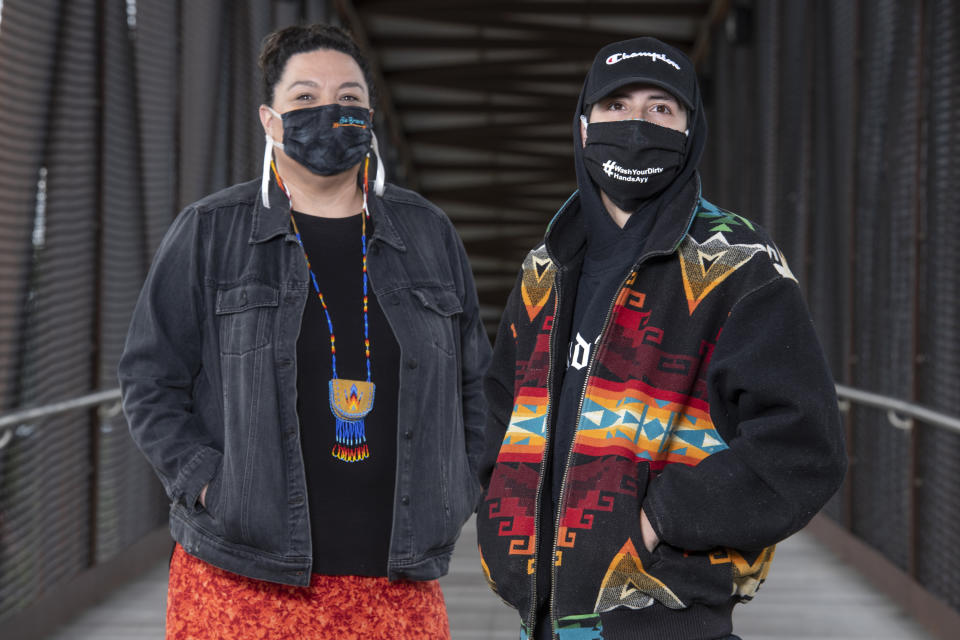 In this photo taken June 16, 2020, Artie Mendoza III and Michelle Mitchell, left, stand for a portrait on the pedestrian bridge overlapping Highway 93 in Pablo, Montana. Mendoza, also known as KiidTruth, is a well known hip-hop artist on the Flathead Indian Reservation. The duo have been using the social media platform TIk Tok to promote hand washing and mask wearing among the youth to prevent the spread of COVID-19 on the reservation. "Our guiding work is for the youth here on the reservation, but that doesn't mean our kids over here can't challenge the kids from Blackfeet," Mitchell said. "They could launch these challenges themselves and take it in to other Indian communities. That would be pretty cool." (AP Photo/Tommy Martino)