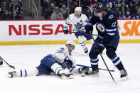Winnipeg Jets' Jansen Harkins (12) and Toronto Maple Leafs' Alexander Kerfoot (15) fight for possession of the puck during the second period of NHL hockey game action in Winnipeg, Manitoba, Sunday, Dec. 5, 2021. (Fred Greenslade/The Canadian Press via AP)