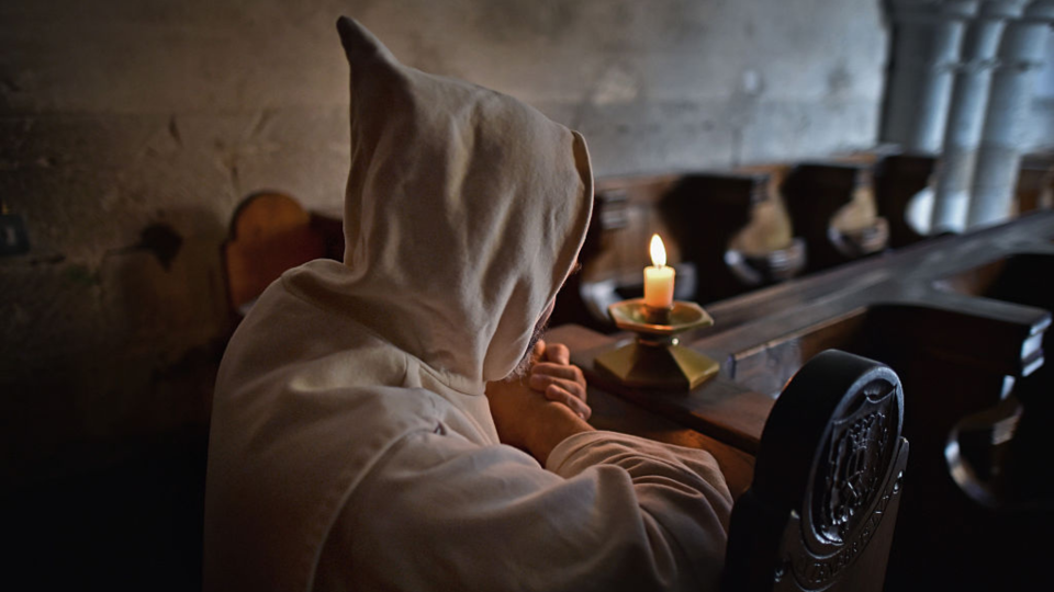 A monk prayers in front of a candle