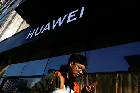 FILE PHOTO: A man uses his phone as he walks past a Huawei shop in Beijing, China, December 19, 2018. REUTERS/Thomas Peter/File Photo