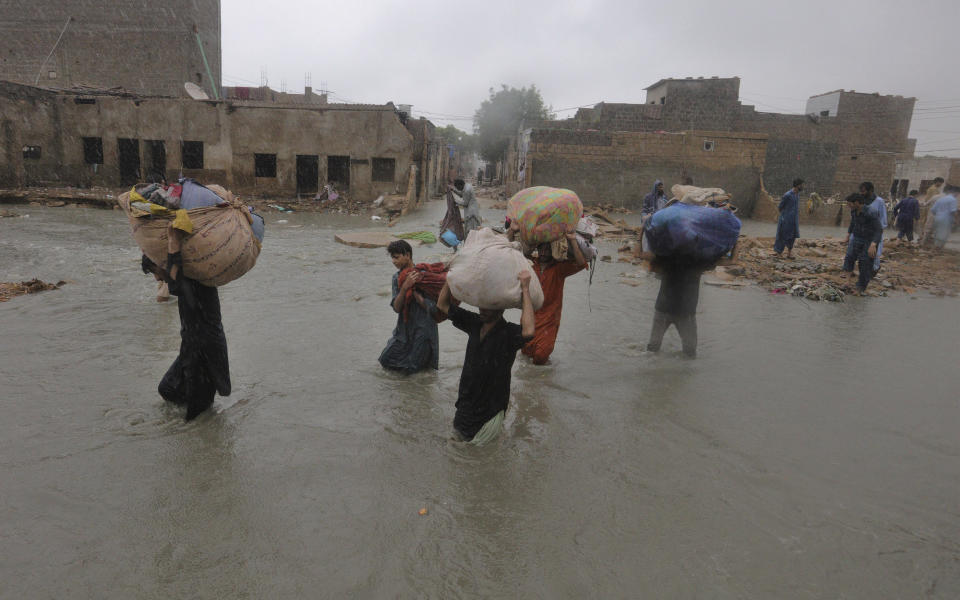 Local residents carry salvaged belongings as they wade through a flooded area during a heavy monsoon rain in Yar Mohammad village near Karachi, Pakistan, Thursday, Aug. 27, 2020. Pakistan's military said it will deploy rescue helicopters to Karachi to transport some 200 families to safety after canal waters flooded the city amid monsoon rains. (AP Photo/Fareed Khan)