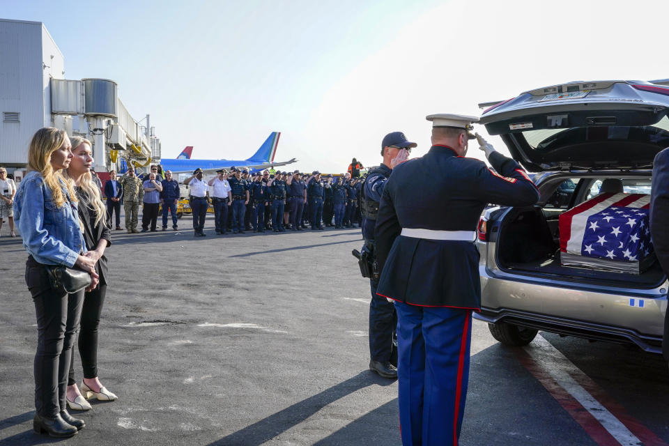 Teresa Irwin, left, sister of Marine Capt. Grady Kurpasi, watches as Marine First Sgt. Timothy La Sage, center, and Port Authority police officer salute after placing his remains into an waiting car at New York's John F. Kennedy International Airport, Friday, May 19, 2023, in New York. The remains of a U.S. Marine veteran who had been missing in Ukraine for more than a year will be returned to his family in eastern North Carolina later Friday, according to the group bringing the remains back to the U.S. (AP Photo/Mary Altaffer)