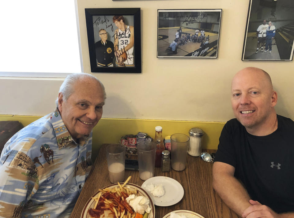 In this 2019 photo provided by UCLA Athletics, Hep Cronin, left, sits with his son UCLA men's basketball coach Mick Cronin, right, at the Wooden's booth at VIP's Cafe in the Tarzana section of Los Angeles where legendary UCLA coach John Wooden used to have breakfast every morning. Mike's dad has become an unlikely celebrity during the Bruins' run to the Final Four in his son's second season in Westwood. (UCLA Athletics via AP)