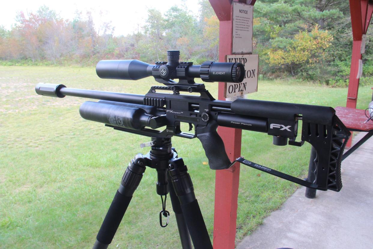 A .35-caliber airgun equipped with a scope rests on a tripod at a shooting range. The airgun is classified as a pre-charged pneumatic, or PCP, and uses stored, compressed air to fire pellets or slugs.