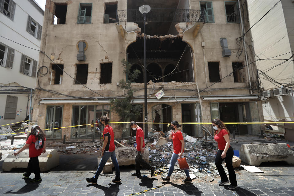 University students who volunteered to help clean damaged homes and give other assistance, pass in front of a building that was damaged by last week's explosion, in Beirut, Lebanon, Tuesday, Aug. 11, 2020. The explosion that tore through Beirut left around a quarter of a million people with homes unfit to live in. But there are no collective shelters, or people sleeping in public parks. That’s because in the absence of the state, residents of Beirut opened their homes to relatives, friends and neighbors. (AP Photo/Hussein Malla)