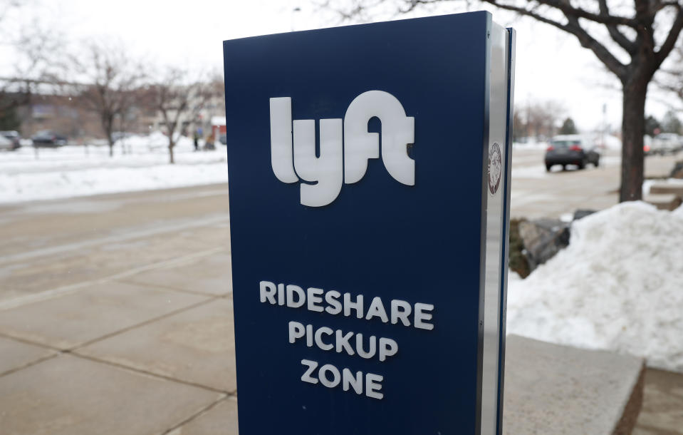 In this Feb. 12, 2020, photograph, a sign for the car sharing service Lyft stands near a pickup zone outside the Pepsi Center in downtown Denver. Just as the coronavirus outbreak has boxed in society, it’s also squeezed high-flying tech companies reliant on people’s freedom to move around and get together. Lyft and rival Uber are turning to deliveries to make up for lost income after ride-hailing screeched to a halt. (AP Photo/David Zalubowski, File)