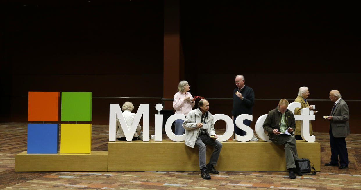 Attendees of Microsoft Corp.'s annual shareholders meeting sit on a Microsoft sign while waiting for the meeting to begin, Wednesday, Dec. 3, 2014, in Bellevue, Wash. The annual meeting was CEO Satya Nadella's first as head of Microsoft. (AP Photo/Ted S. Warren)