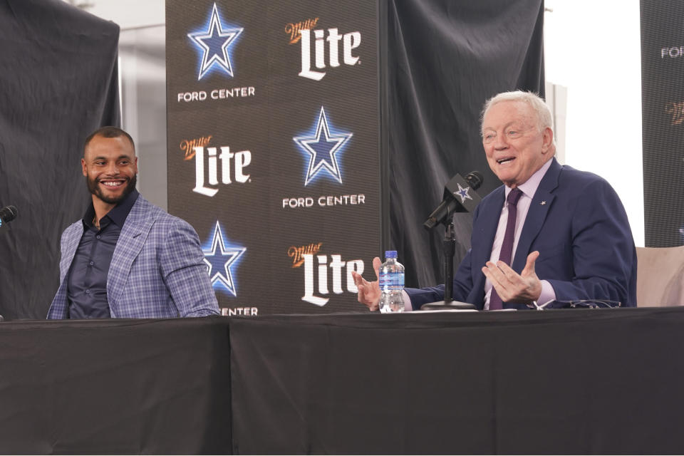 Dallas Cowboys quarterback Dak Prescott, left, looks on and smiles as team owner Jerry Jones speaks during a news conference at the team's NFL football practice facility in Frisco, Texas, Wednesday, March 10, 2021. The Cowboys and Prescott have finally agreed on the richest contract in club history, two years after negotiations began with the star quarterback. (AP Photo/LM Otero)