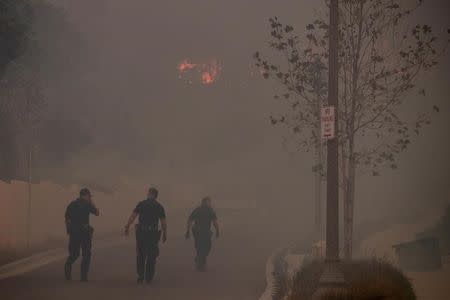 FILE PHOTO: Ventura policemen rush to check a home in a burning neighborhood as strong winds carry a wildfire into Ventura, California, U.S. on December 5, 2017. REUTERS/Mike Blake/File Photo