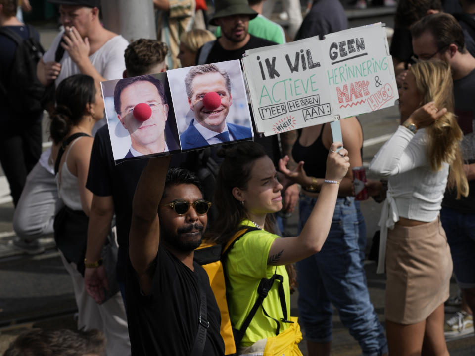 A person carries a placard depicting caretaker prime minister Mark Rutte and deputy prime minister Hugo de Jonge as clowns during a protest of organizers and fans of music festivals against the government's COVID-19 restrictions on large-scale outdoor events in Amsterdam, Netherlands, Saturday, Sept. 11, 2021. On Saturday, the festivals came to music fans as hundreds of performers and festival organizers called again for demonstration marches through Dutch cities to protest what they argue are unfair restrictions that have forced the cancellation of summer festivals and other events. (AP Photo/Peter Dejong)