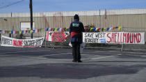 A person looks at signs hanging in a parking lot, the only undeveloped portion of the shellmound in West Berkeley where ancestors of today's Ohlone people established the first human settlement on the shores of the San Francisco Bay, in Berkeley, Calif., Wednesday, March 13, 2024. Berkeley's City Council voted unanimously Tuesday, March 12, 2024, to adopt an ordinance giving the title of the land to the Sogorea Te' Land Trust, a women-led, San Francisco Bay Area collective that works to return land to Indigenous people and that raised the funds needed to reach the agreement. (AP Photo/Jeff Chiu)