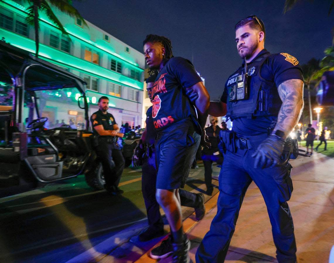 Miami Beach police officers escort a man to an awaiting police transport vehicle on Ocean Drive across from the Avalon Hotel during spring break on Miami Beach, Florida on Saturday, March 16, 2024.