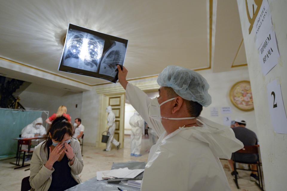 A medical specialist, wearing a protective suit, checks a young woman's, lung X-ray inside a restaurant that was converted into a clinic in Bishkek, Kyrgyzstan, Wednesday, July 22, 2020. The restaurant in the center of Bishkek was converted into a night-time clinic to support the country's health care system, struggling with the coronavirus outbreak. Doctors and nurses from other facilities work there and treat people between 8 p.m. and 8 a.m. (AP Photo/Vladimir Voronin)