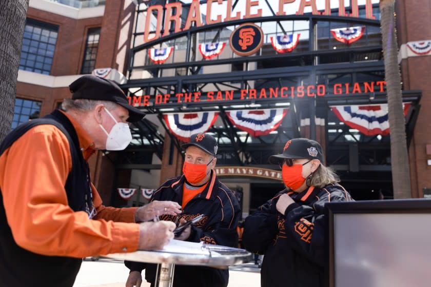 SAN FRANCISCO, CALIFORNIA - APRIL 09: San Francisco Giants fans Dave Harding of San Leandro, center, and his wife, Nancy Faltisek, check in at one of the vaccination/negative test verification booths to show the proof of their COVID-19 vaccinations before being admitted to Oracle Park at the Giants' season home opener on Friday, April 9, 2021, in San Francisco, Calif. (Dai Sugano/Bay Area News Group)