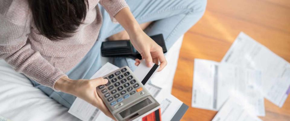 Young woman seen from above, sitting with calculator and pile of bills.