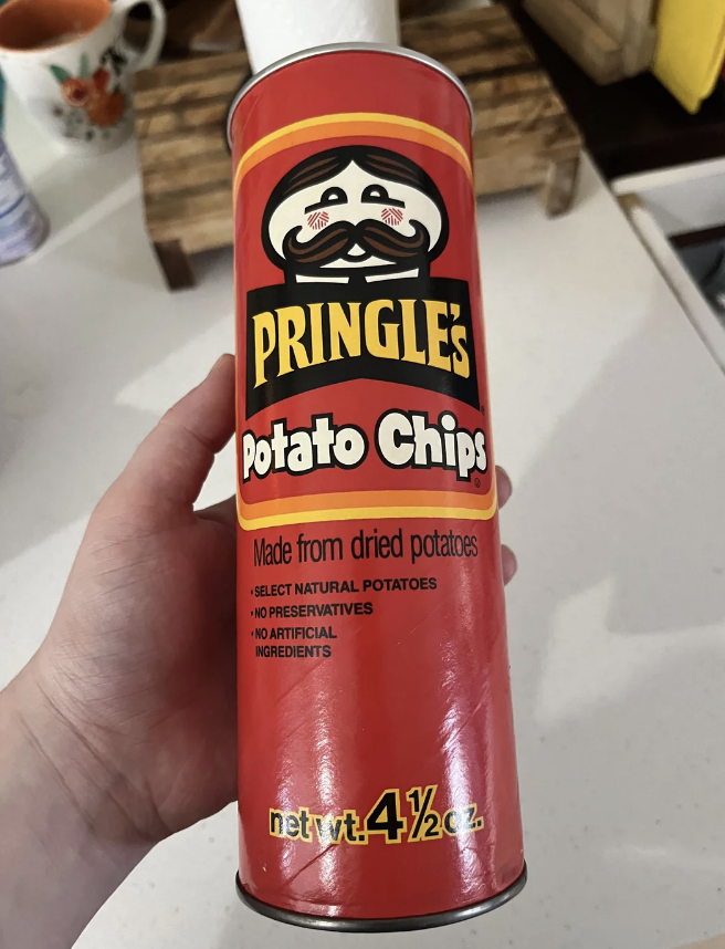 A hand holds a Pringle's Potato Chips can. The label says: "Made from dried potatoes. Select natural potatoes. No preservatives. No artificial ingredients."