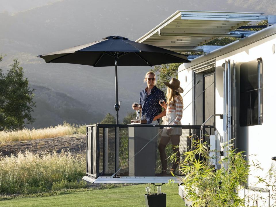 two people standing on the balcony of the 2022 Living Vehicle trailer