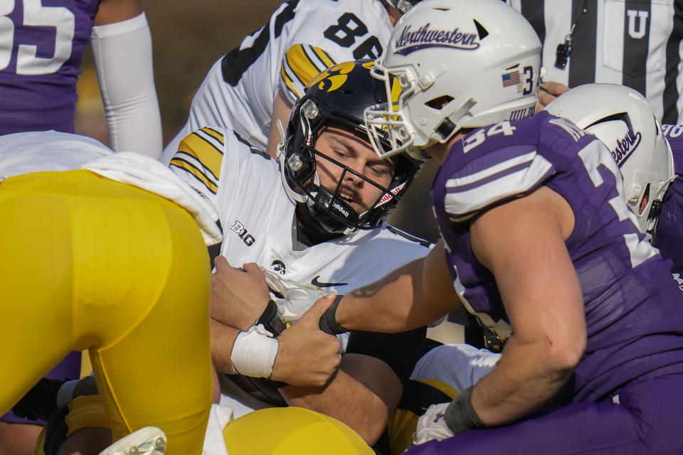 Iowa quarterback Deacon Hill, center, clings to the ball as he is tackled by Northwestern players during the first half of an NCAA college football game Saturday, Nov. 4, 2023, at Wrigley Field in Chicago. (AP Photo/Erin Hooley)