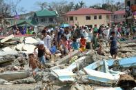 Residents walk through debris as they rush to a rescue helicopter delivering relief foods in Hernani town, Eastern Samar province, central Philippines on November 11, 2013