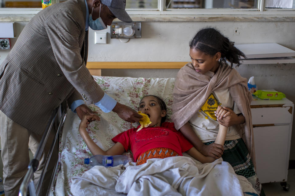 Akhberet Tadesa, 15, who is unable to feed herself and hasn't spoken or walked unaided since a shell exploding near her home left her in an apparent state of mental shock, is aided by her father Tadese Gebremedhin, left, and sister Fana, 13, right, at the Ayder Referral Hospital in Mekele, in the Tigray region of northern Ethiopia, on Thursday, May 6, 2021. As the Tigray People’s Liberation Front and the government forces fight, civilians, and especially children, are suffering heavily. (AP Photo/Ben Curtis)