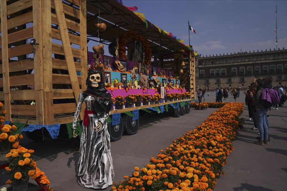 Personas posan para las fotos cerca de una figura de una catrina al lado de un vagón por la celebración del Día de Muertos en el Zócalo, la principal plaza de Ciudad de México, el martes 31 de octubre de 2023. (AP Foto/Marco Ugarte)