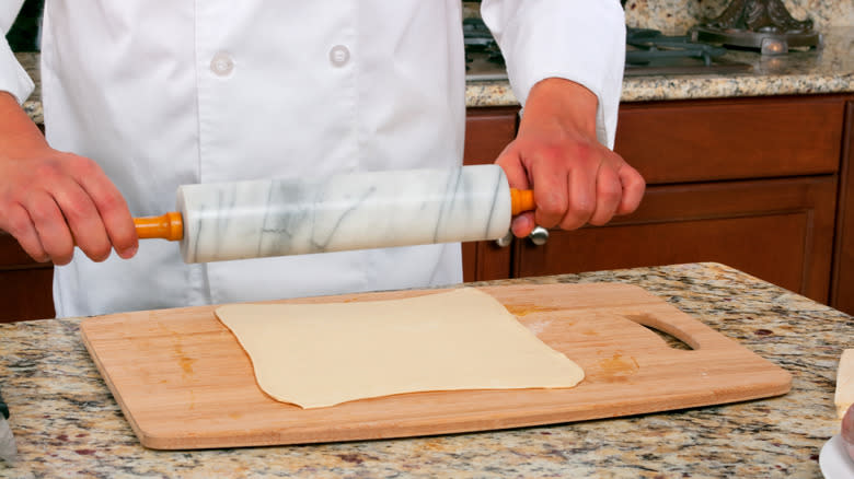 Chef rolling dough on cutting board