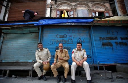 Indian policemen sit in front of closed shops during restrictions in Srinagar