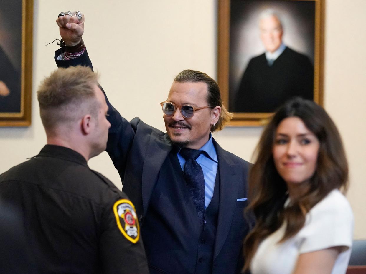 A picture of Johnny Depp in court raising his fist in the air and smiling.