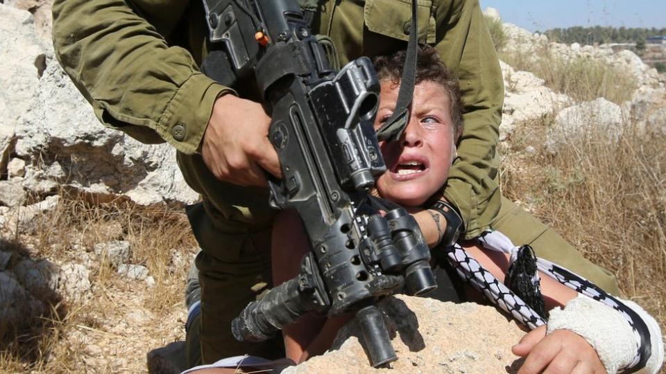 Un soldado israelí armado con un fusil retiene a un niño por el cuello