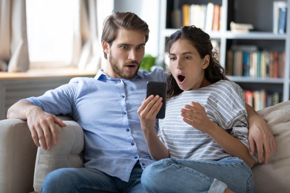 Couple sharing a smartphone and looking amazed at what they see.