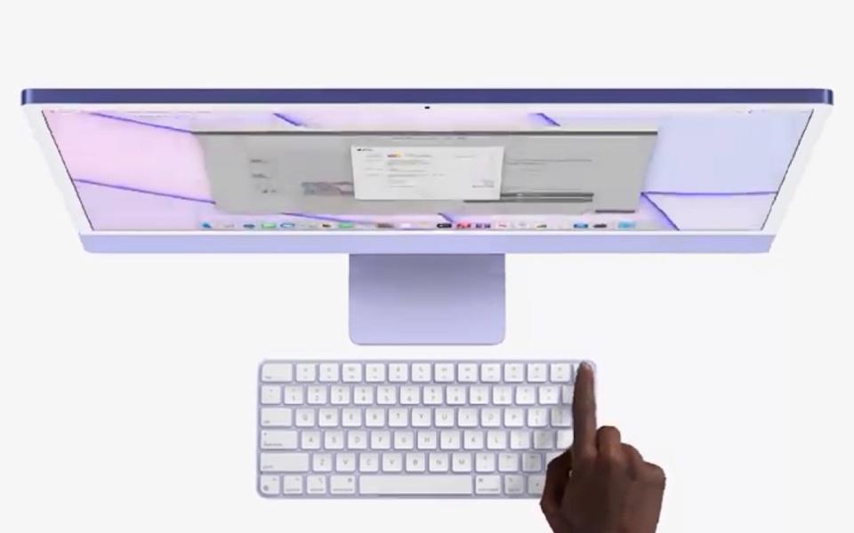 A top-down view as a finger reaches out to touch the fingerprint sensor in the top right hand corner of a lilac-purple iMac - Apple