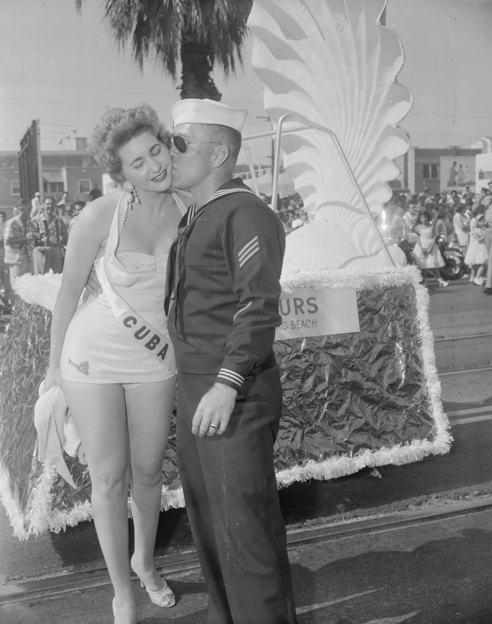 Long Beach, California: A glutton for beauty is this sailor who volunteered to be the mobile force for "Miss Cuba's" float in the "Miss Universe" parade here today. At the end of the two mile hot treck the young sailor was rewarded with a kiss.