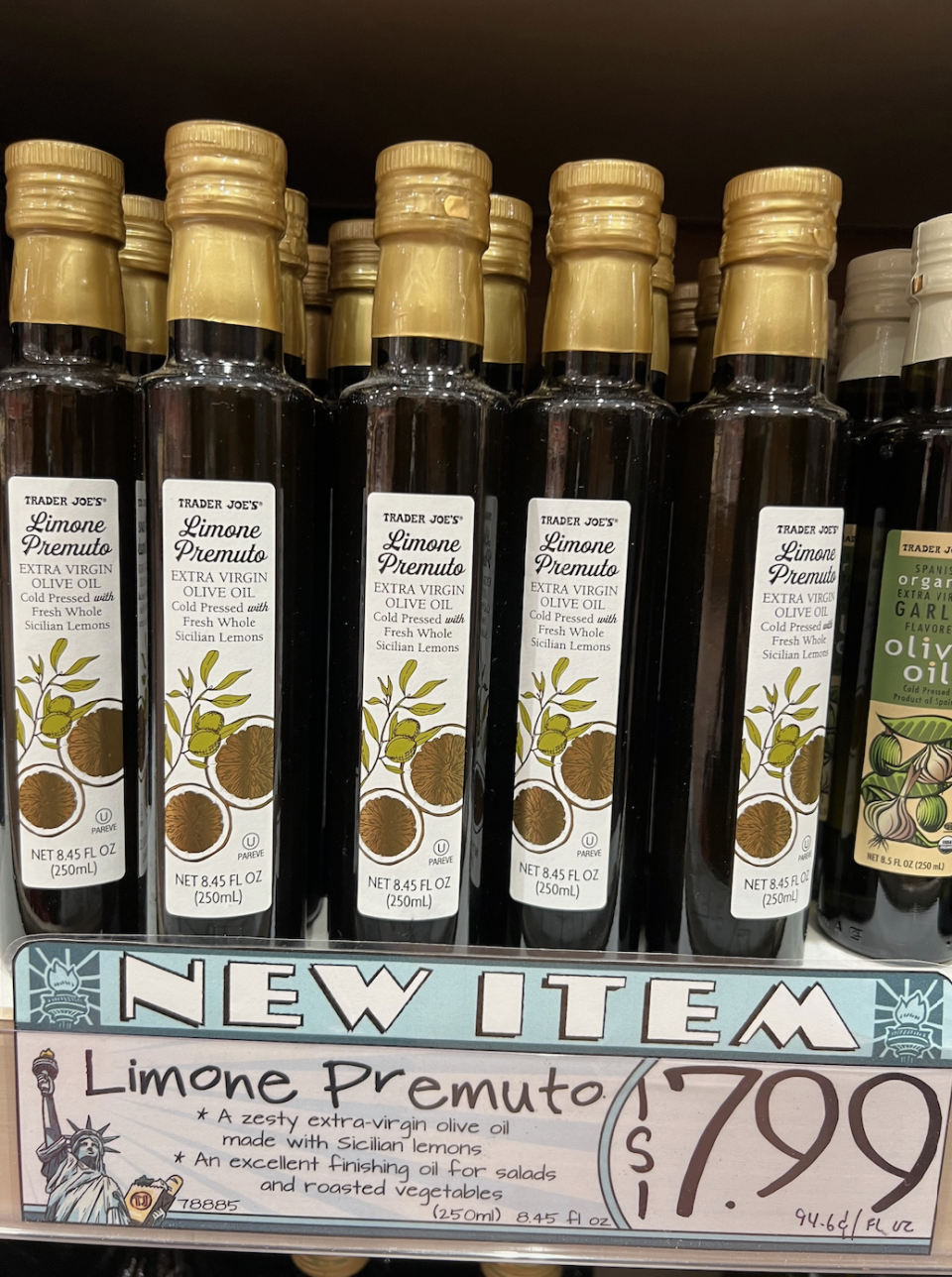 Trader Joe's Limone Premuto Extra-Virgin Olive Oil bottles on a store shelf with a sign highlighting the price of $7.99