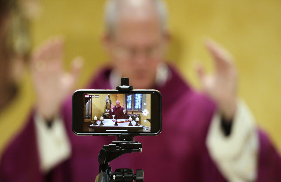 A cell phone is used to live stream mass by Archbishop Paul D. Etienne at St. James Cathedral, the Cathedral for the Catholic Archdiocese of Seattle, where open masses have been suspended because of the coronavirus outbreak, Saturday, March 28, 2020, in Seattle. The church remains open for people to sit in the sanctuary in the mornings and is live streaming a mass every morning. (AP Photo/Elaine Thompson)