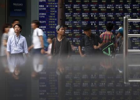 Pedestrians standing in front of an electronic board showing the various stock prices outside a brokerage are reflected in a polished stone surface, in Tokyo August 13, 2014. REUTERS/Yuya Shino