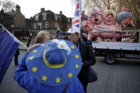 A remain in the European Union, anti-brexit sculpture is displayed as a protester wearing a European flag design hat stands demonstrating in the foreground across the street from the House of Parliament in London, Tuesday, Dec. 11, 2018. Top European Union officials are ruling out any renegotiation of the divorce agreement with Britain as Prime Minister Theresa May fights to save her Brexit deal by lobbying leaders in Europe's capitals. (AP Photo/Matt Dunham)