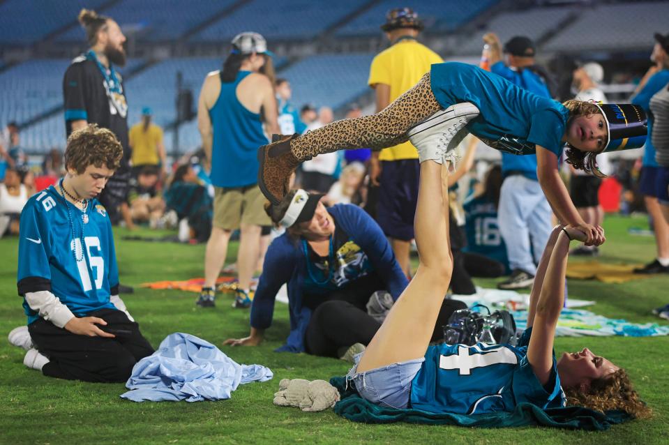 Makenzie Watrous, bottom, plays with her half sister, Piper Davis, 6, as mom Mandy Watrous, center back, and brother Carson Watrous, 13, left, sit on the field during the Duuval Draft Party on Thursday at EverBank Stadium in Jacksonville.