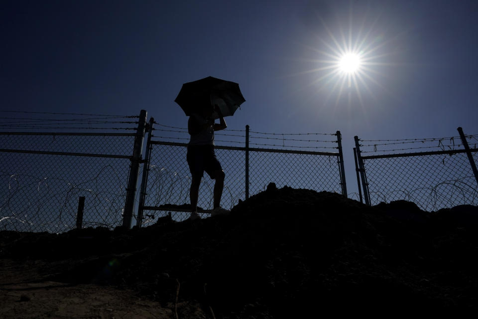 Magali Urbina shields herself from the sun with an umbrella as she watches as the state installs large buoys to be used as a border barrier along the Rio Grande along her farm near Eagle Pass, Texas, Monday, July 10, 2023. Texas Republican Gov. Greg Abbott has escalated measures to keep migrants from entering the U.S. He's pushing legal boundaries along the border with Mexico to install razor wire, deploy massive buoys on the Rio Grande and bulldozing border islands in the river. (AP Photo/Eric Gay)