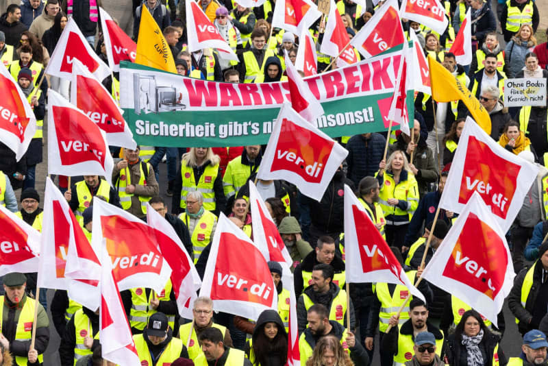 Strikers march from the Lufthansa Aviation Center to Terminal 1 with banners and Verdi flags during a protest.  With renewed warning strikes by several professional groups, the Verdi union is paralyzing important parts of German air traffic on Thursday and Friday. Lando Hass/dpa