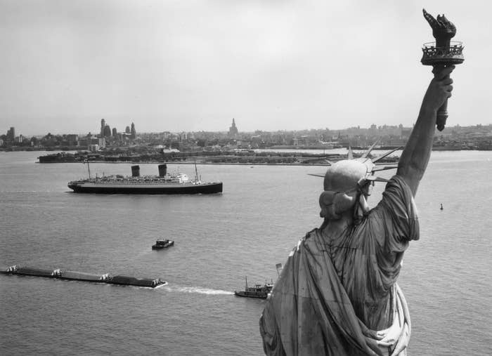 Statue of Liberty in foreground with a ship in the harbor and the New York City skyline in the background