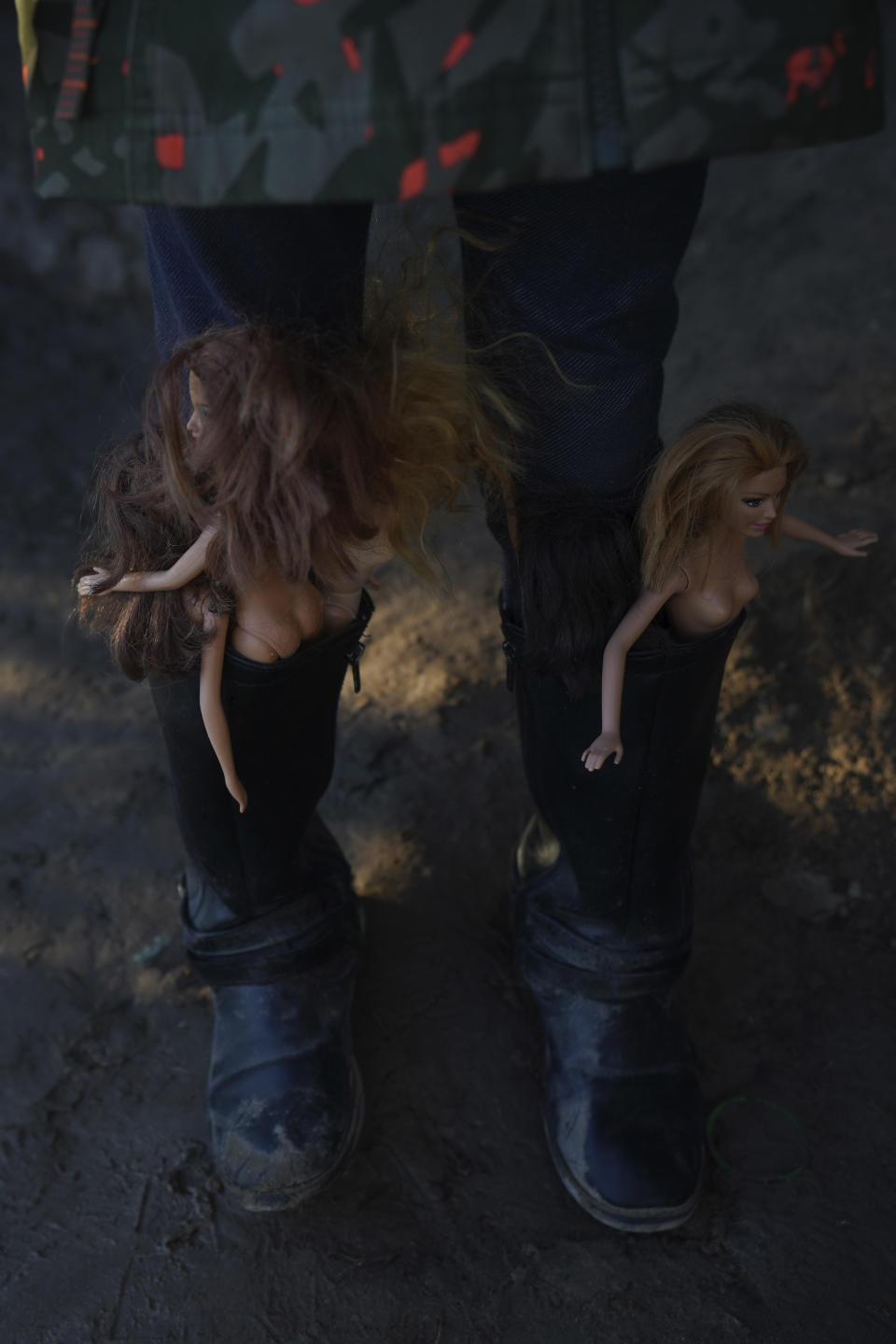 A girl with Barbie dolls stuffed in her boots waits with other children to cross the Rio Grande river with their parents as they stand on the bank of the Rio Grande river in Ciudad Acuna, Mexico, at dawn Thursday, Sept. 23, 2021, across the border from Del Rio, Texas. (AP Photo/Fernando Llano)