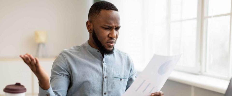 Paper Problems. Shocked African Businessman Looking Through Negative Financial Report And Tax Bills Working Sitting In Office. Bank Financial Issues Concept. Selective Focus