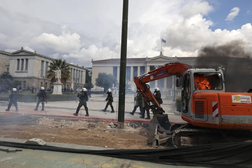 A small excavator is on fire as riot police operate against protesters during clashes outside the headquarters of Athens University, Greece, Sunday, March 5, 2023. Thousands protesters, take part in rallies around the country for fifth day, protesting the conditions that led the deaths of dozens of people late Tuesday, in Greece's worst recorded rail accident. (AP Photo/Yorgos Karahalis)