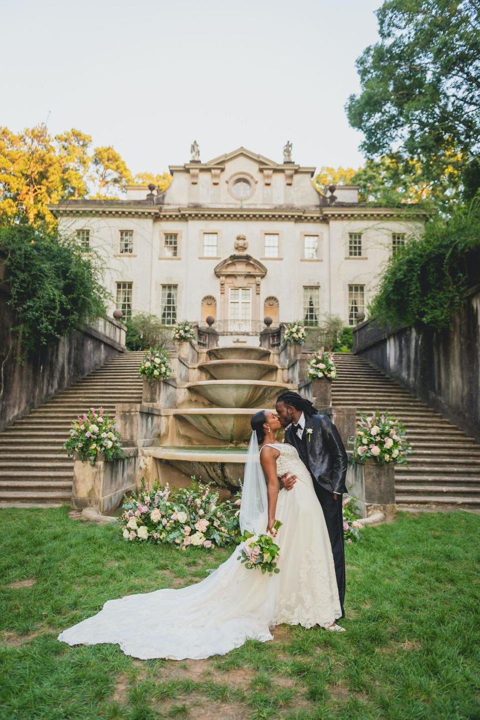 A bride and groom kiss in front of a mansion.