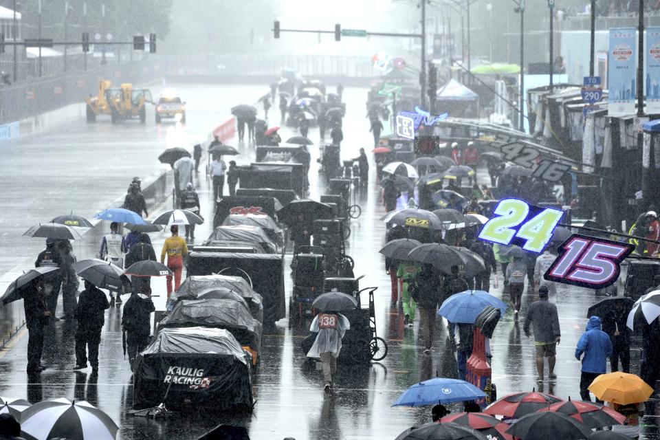 People walk along pit row in the rain before a NASCAR Cup Series auto race at the Grant Park 220 Sunday, July 2, 2023, in Chicago. (AP Photo/Morry Gash)