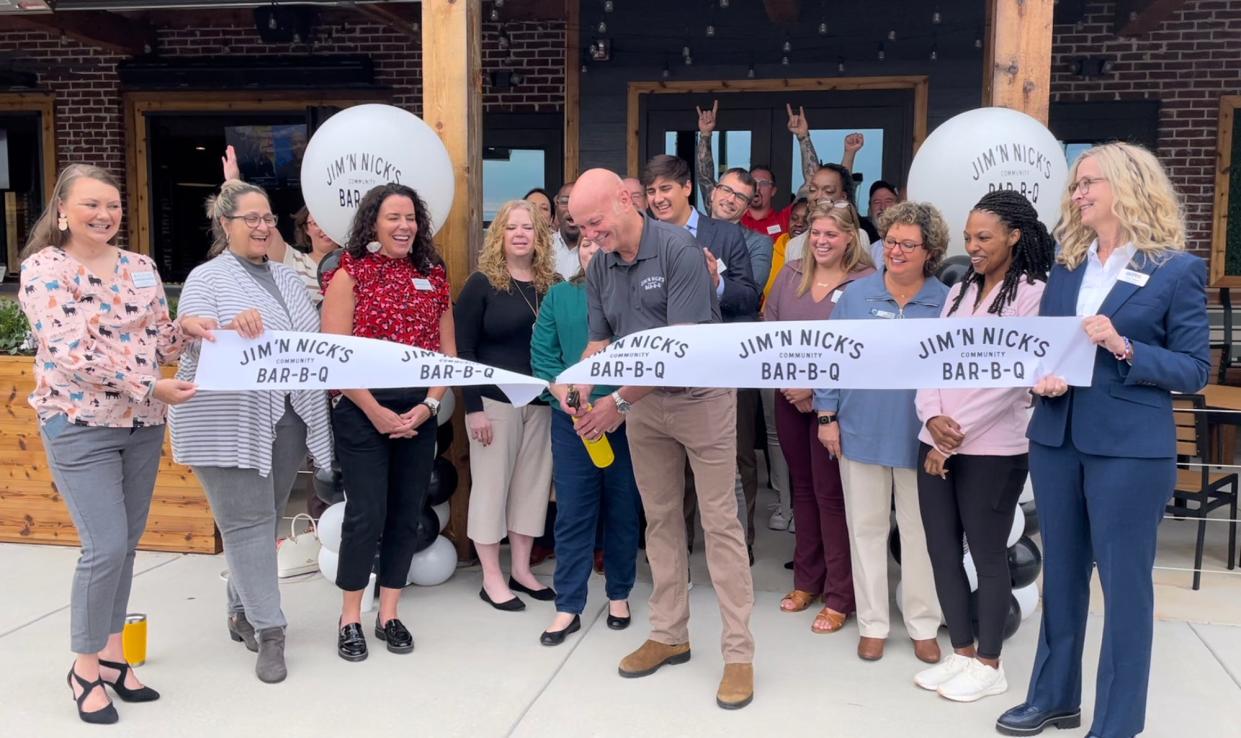 Jim 'N Nick's Community Bar-B-Q president and COO Brian Lyman (center) uses a propane torch to cut the ribbon at the Alabama-based restaurant chain's Athens, Ga. location on Wednesday, Oct. 11, 2023.